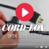 A pair of hands fastens a Coil'n'Carry® Strap around a black electrical cord with a plug, showing the Coil'n'Carry® logo and video player controls at the bottom.