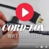 Close-up of hands attaching a Coil'n'Carry® Strap to a power cord. A large red play button overlays the image, with the Coil'n'Carry® name and branding text displayed over the strap and cord.