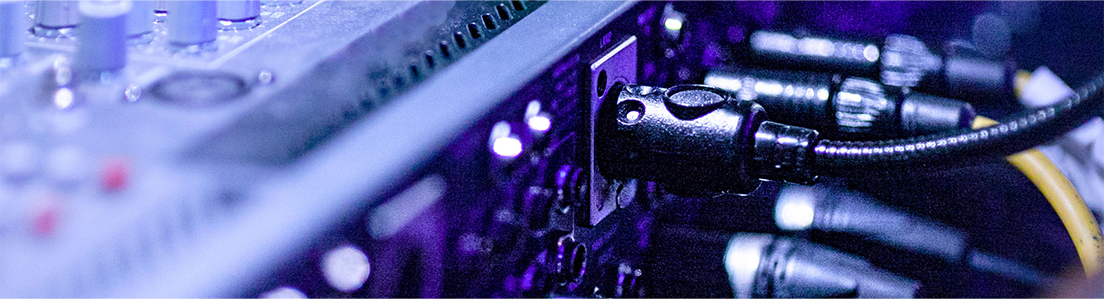 Close up of audio cables plugged into the back of sound equipment in a dimly lit environment with purple and blue lighting creating a high tech studio like atmosphere