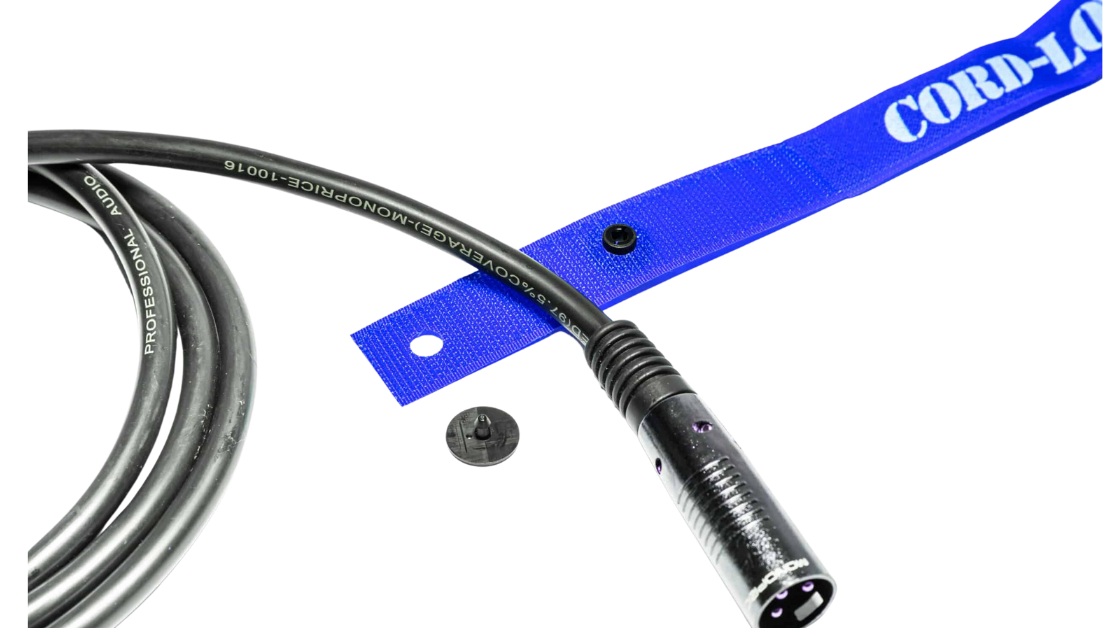 A black audio cable with an XLR connector lies next to a blue strap labeled CORDLO and a small black button all on a white background TFI Custom Fabrication A black audio cable with an XLR connector lies next to a blue strap labeled CORD LO and a small black button all on a white background