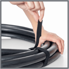 A hand secures a black hook and loop strap around a bundle of thick black cables keeping them organized