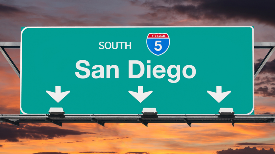 Green freeway sign reading SOUTH Interstate 5 San Diego with three white arrows pointing down set against a sunset sky