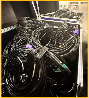 Coiled audio or data cables organized in a black storage case with labeled tags and various colored connectors visible on the ends