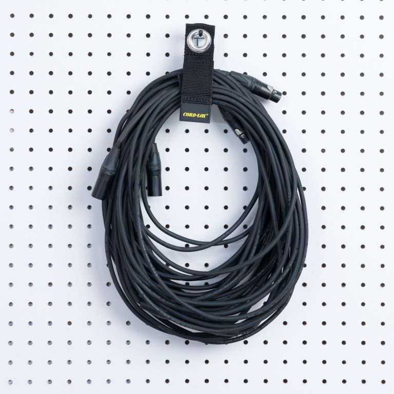A long black audio cable hangs neatly on a white pegboard secured by a Cord Lox® HangMaster™ ProSeries Heavy Duty Hook  Loop Cable Hanging  Storage Strap with metal grommet for organized XLR cable storage