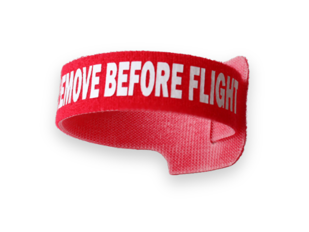 A red fabric wristband with the white text REMOVE BEFORE FLIGHT printed on it shown against a white background TFI Custom Fabrication A red fabric wristband with the white text REMOVE BEFORE FLIGHT printed on it shown against a white background