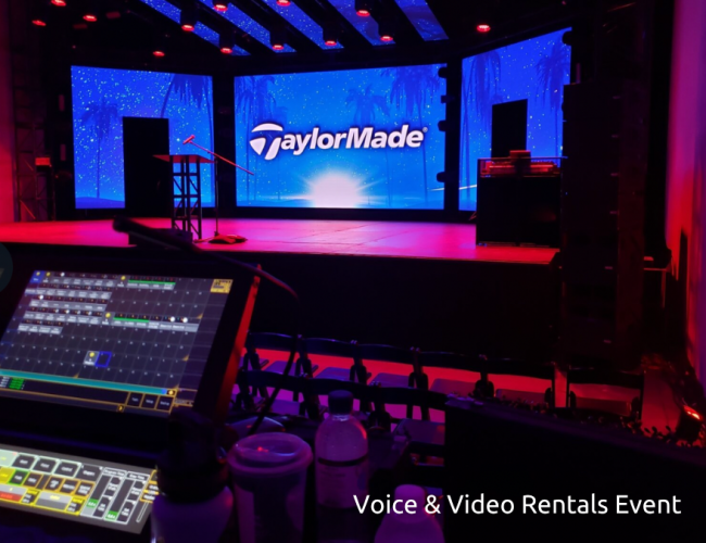 A stage set for a TaylorMade event features a large screen with the company logo podium and sound equipment viewed from behind an audiovisual control panel Text reads Voice Video Rentals Event TFI Custom Fabrication A stage set for a TaylorMade event features a large screen with the company logo podium and sound equipment viewed from behind an audio visual control panel Text reads Voice Video Rentals Event